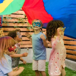 Children with face paint play under a colourful parachute to illustrate an article titled: Top 5 Children’s Birthday Party Themes